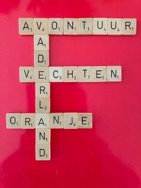 Scrabbleletters op een rode ondergrond die de woorden avontuur, vaderland, vechten en Oranje vormen