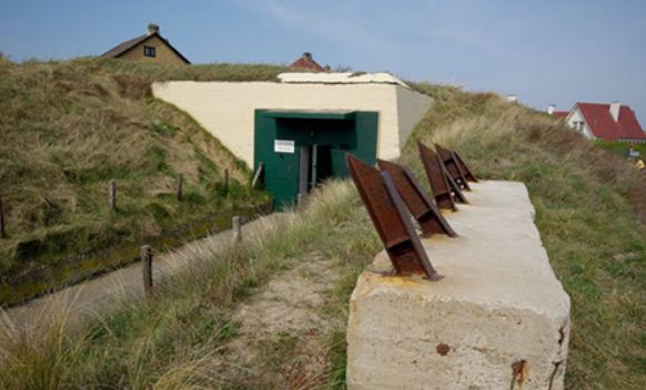 De met duingras begroeide munitiebunker FL246, met de groene toegangsdeur en een gemetselde borstwering ervoor
