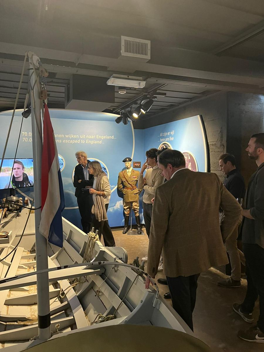 Bezoekers in de museumzaal bij de reddingsboot, met de Nederlandse vlag en de vitrines op de achtergrond