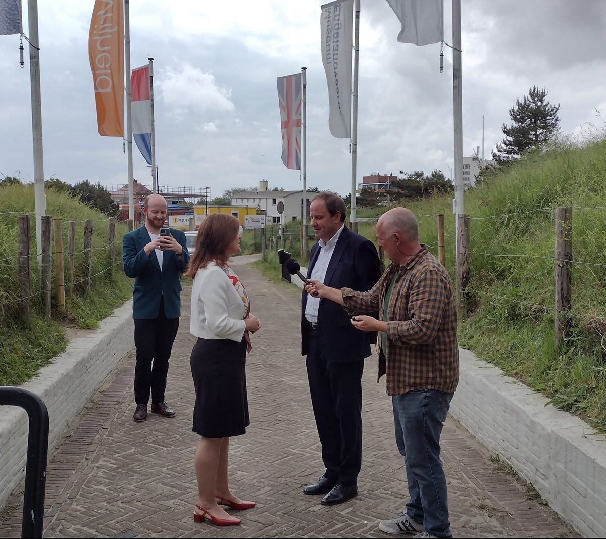 Vier mensen in gesprek op het pad naar het museum, met vlaggen langs de route