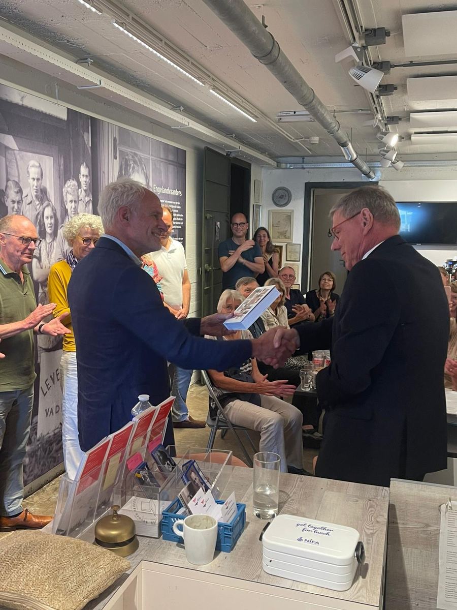 Overhandiging van het eerste exemplaar van het boek in de museumzaal, met publiek eromheen