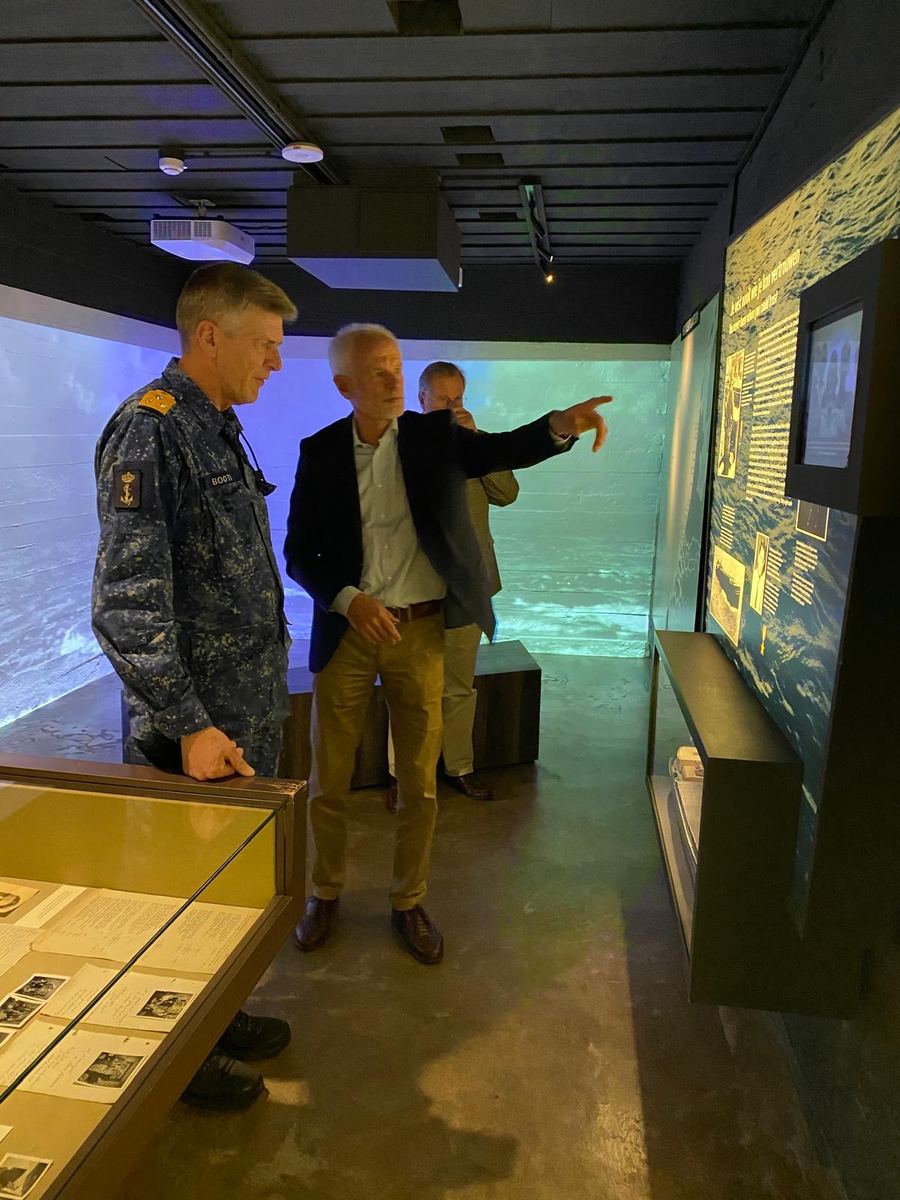 Twee mannen in de museumzaal, één in camouflage-uniform, kijken naar een vitrine