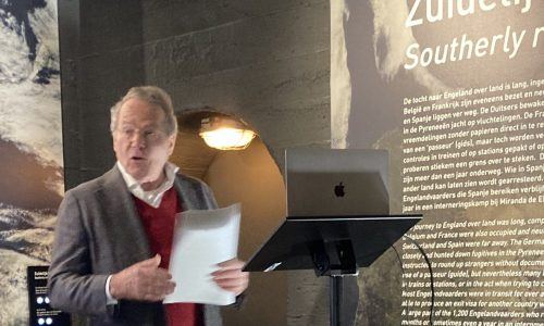 Spreker achter een katheder met laptop, voor het museumpaneel over de zuidelijke route