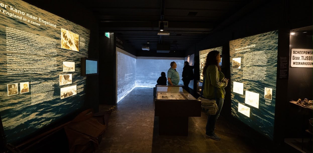 Bezoekers in de zaal over de overtocht, tussen wanden met de zee en de verhalen van Engelandvaarders, zoals Per kano naar Engeland